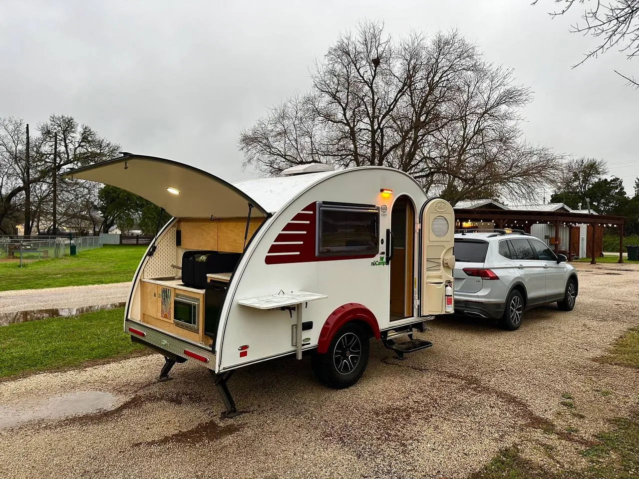 Compact teardrop trailer with rear kitchen hatch open at a campsite